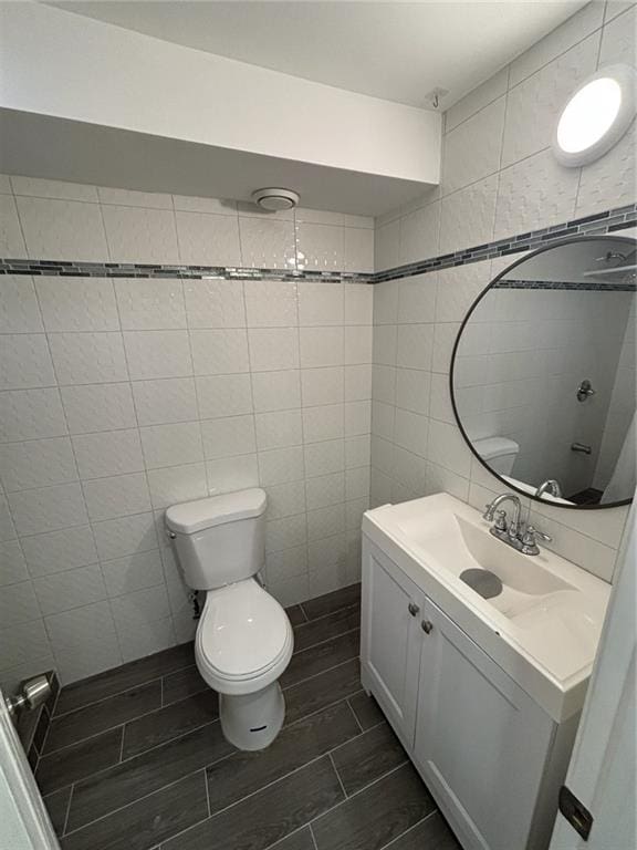 bathroom with toilet, vanity, tile walls, and wood tiled floor