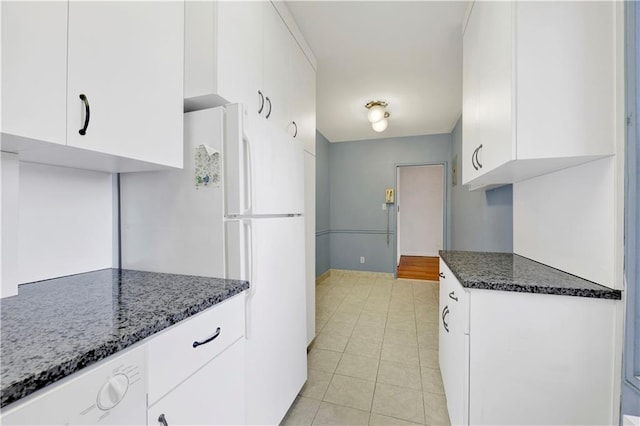kitchen featuring freestanding refrigerator, baseboards, white cabinets, dark stone countertops, and light tile patterned floors