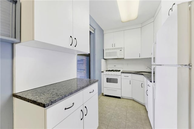 kitchen with a sink, light tile patterned floors, white cabinets, dark stone countertops, and white appliances