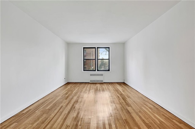 unfurnished room featuring light wood finished floors, radiator heating unit, and baseboards