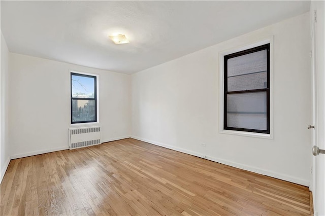 empty room with radiator heating unit, baseboards, and wood-type flooring