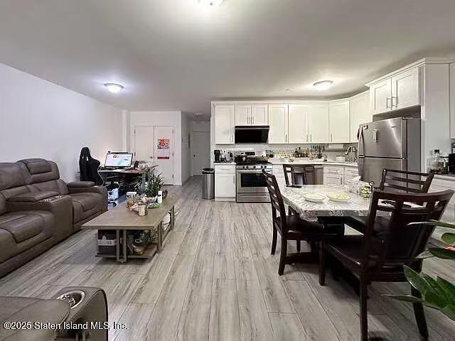 interior space featuring light wood-style flooring, stainless steel appliances, white cabinetry, open floor plan, and light countertops