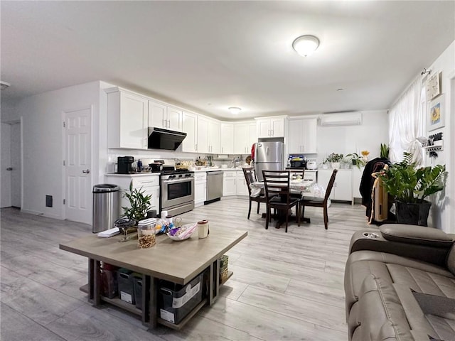 kitchen featuring a wall unit AC, light wood finished floors, light countertops, appliances with stainless steel finishes, and white cabinets