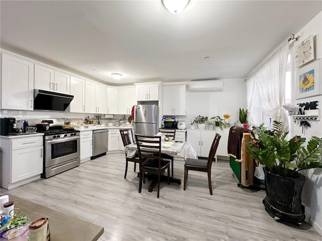 kitchen featuring appliances with stainless steel finishes, light countertops, light wood-type flooring, white cabinetry, and a wall mounted AC