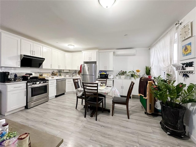 kitchen with a wall mounted AC, stainless steel appliances, light wood-style flooring, light countertops, and white cabinets