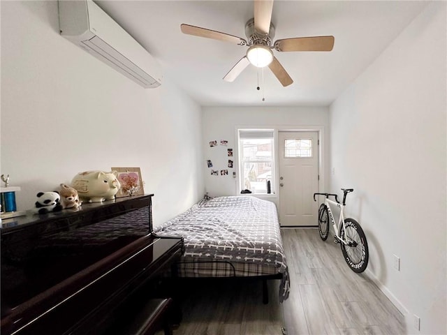 bedroom with light wood-type flooring, a wall mounted air conditioner, ceiling fan, and baseboards