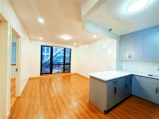 kitchen featuring light wood-style flooring, gray cabinets, decorative light fixtures, and a peninsula