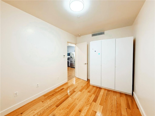 unfurnished bedroom featuring light hardwood / wood-style flooring, stainless steel refrigerator with ice dispenser, and a closet