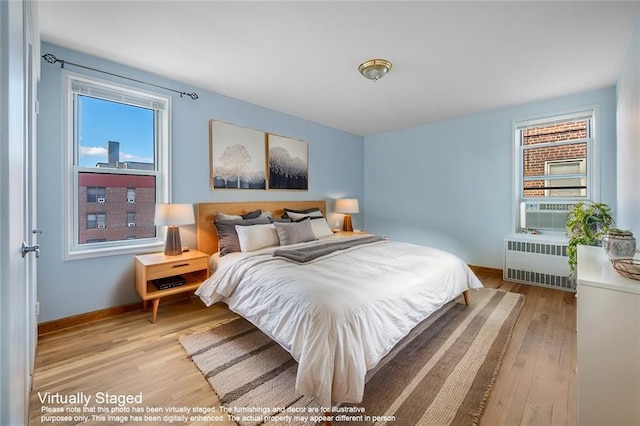 bedroom with cooling unit, radiator, and light wood-type flooring