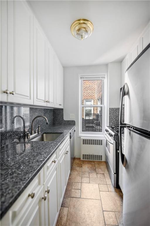 kitchen with appliances with stainless steel finishes, radiator, sink, and white cabinets