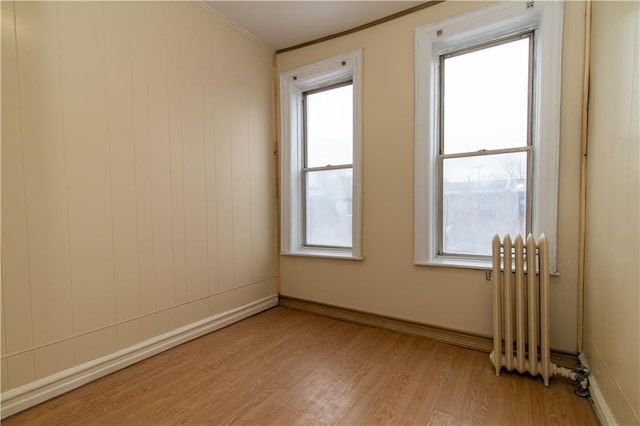 empty room with light hardwood / wood-style flooring, crown molding, and radiator heating unit