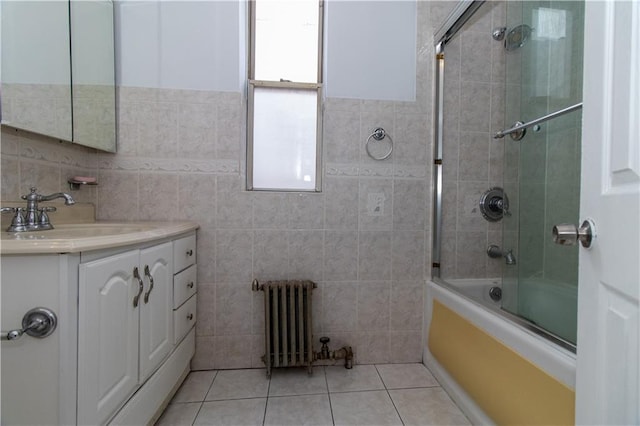 bathroom with combined bath / shower with glass door, radiator heating unit, tile walls, vanity, and tile patterned floors