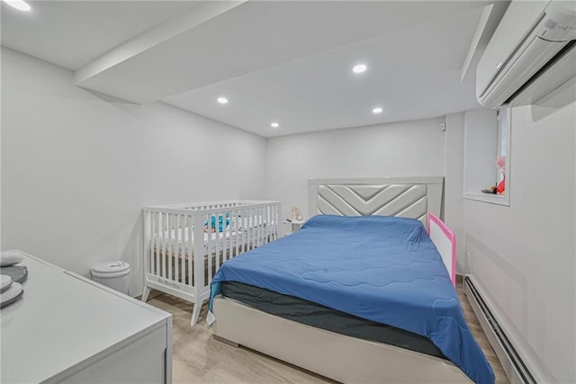 bedroom with a baseboard heating unit, a wall mounted AC, and light hardwood / wood-style floors