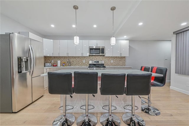 kitchen featuring a breakfast bar, appliances with stainless steel finishes, white cabinetry, a center island, and decorative light fixtures