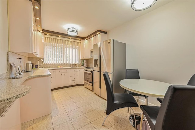 kitchen with sink, light tile patterned floors, appliances with stainless steel finishes, white cabinets, and decorative backsplash