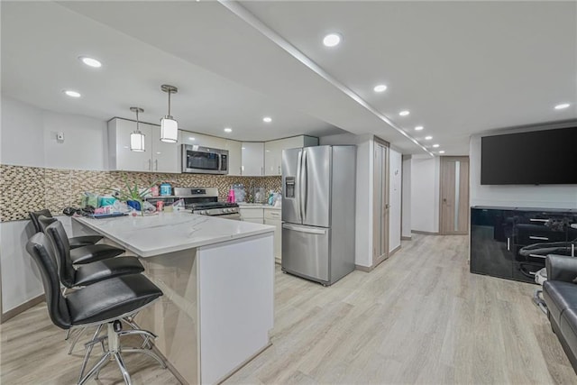 kitchen featuring appliances with stainless steel finishes, white cabinetry, hanging light fixtures, a kitchen bar, and kitchen peninsula