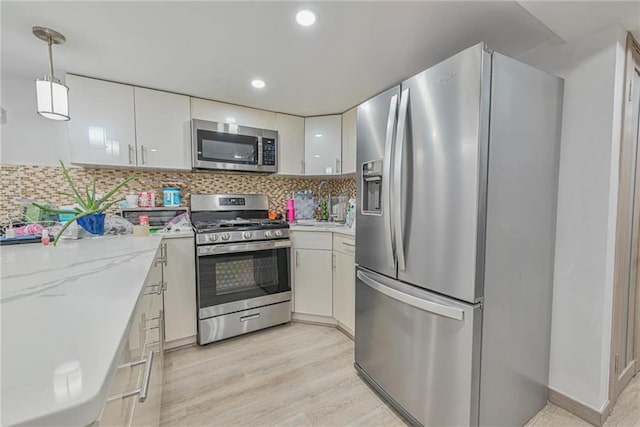 kitchen with white cabinetry, decorative light fixtures, light wood-type flooring, stainless steel appliances, and decorative backsplash