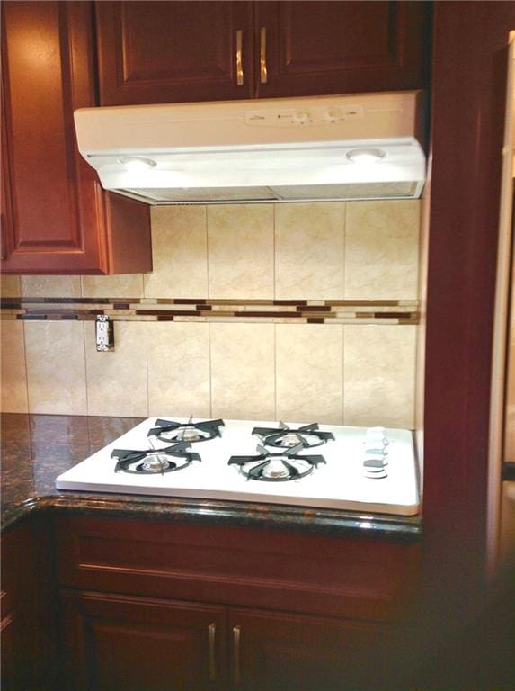 kitchen with dark countertops, white gas stovetop, under cabinet range hood, and decorative backsplash