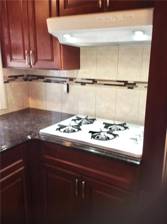 kitchen featuring white gas stovetop, dark brown cabinets, tasteful backsplash, and under cabinet range hood