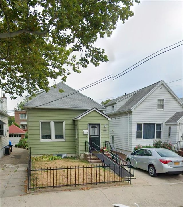 bungalow-style home with a fenced front yard, roof with shingles, and entry steps