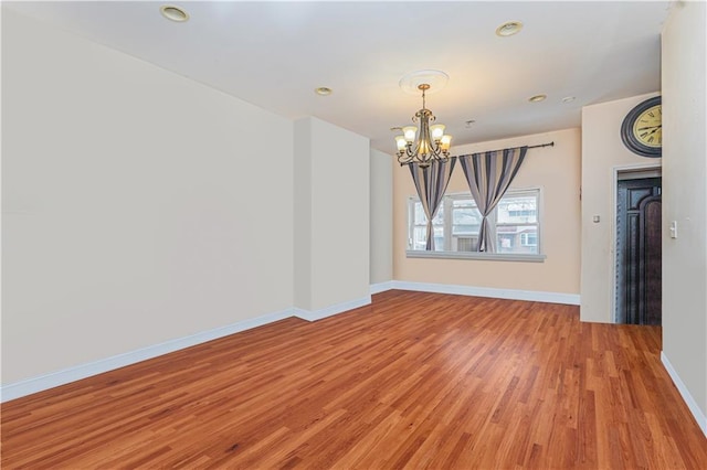 spare room featuring light wood-style flooring, baseboards, a notable chandelier, and recessed lighting