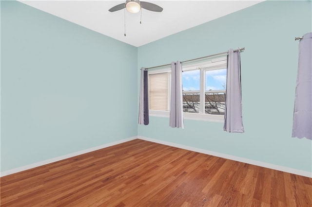 empty room with wood finished floors, a ceiling fan, and baseboards