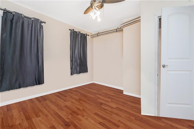 empty room with wood finished floors, a ceiling fan, and baseboards