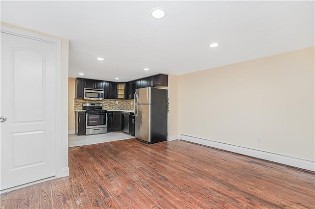 kitchen featuring appliances with stainless steel finishes, dark cabinets, wood finished floors, a baseboard heating unit, and backsplash