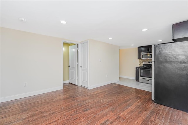 kitchen with baseboards, dark wood-type flooring, decorative backsplash, stainless steel appliances, and dark cabinetry