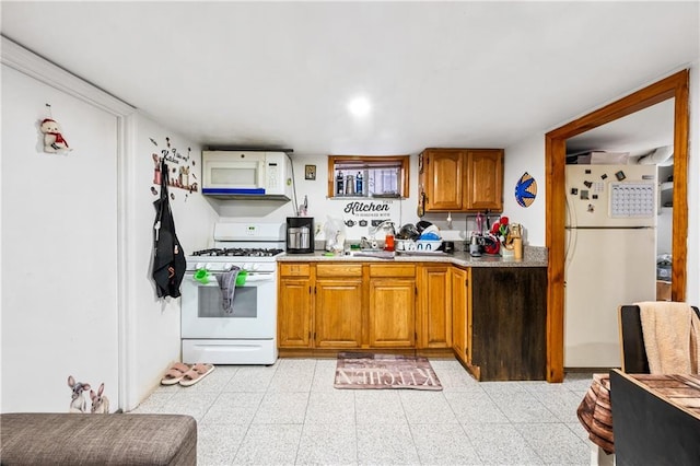 kitchen featuring light floors, light countertops, brown cabinetry, white appliances, and a sink