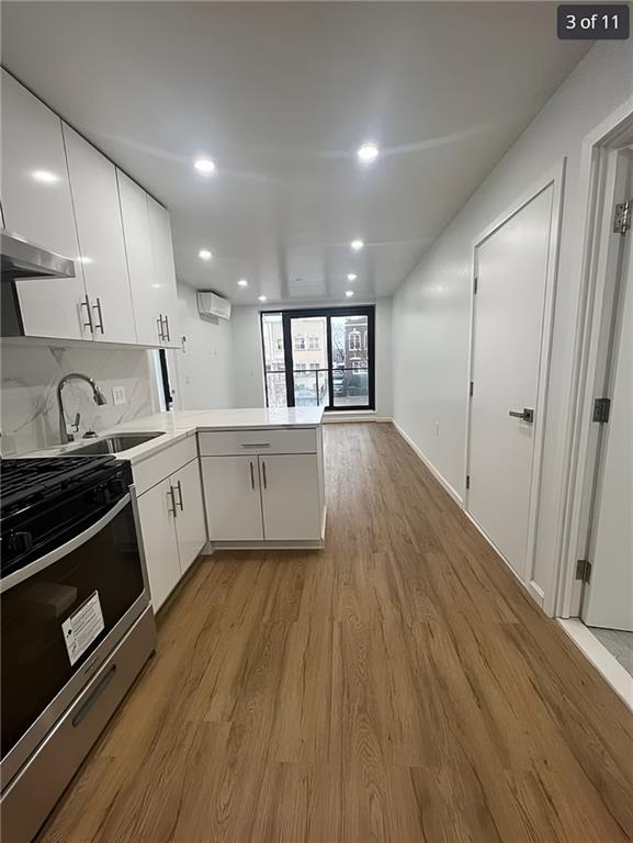 kitchen featuring stainless steel gas range oven, a peninsula, light countertops, white cabinetry, and a sink