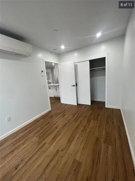 unfurnished bedroom with a wall mounted AC, wood finished floors, baseboards, a closet, and recessed lighting
