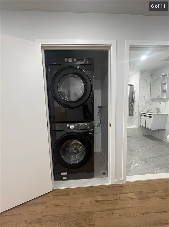 laundry area with stacked washer / drying machine and wood finished floors