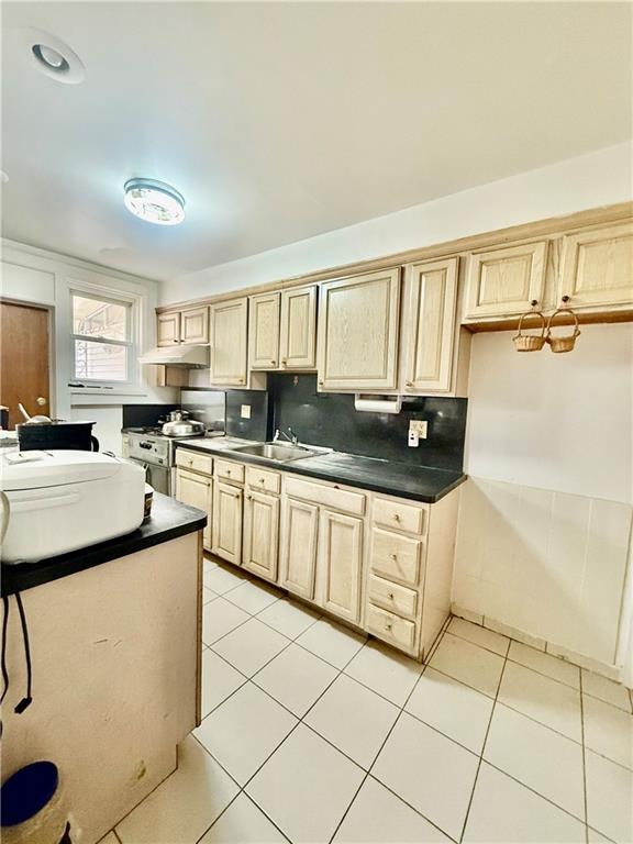 kitchen with under cabinet range hood, dark countertops, stainless steel gas range oven, and light tile patterned floors