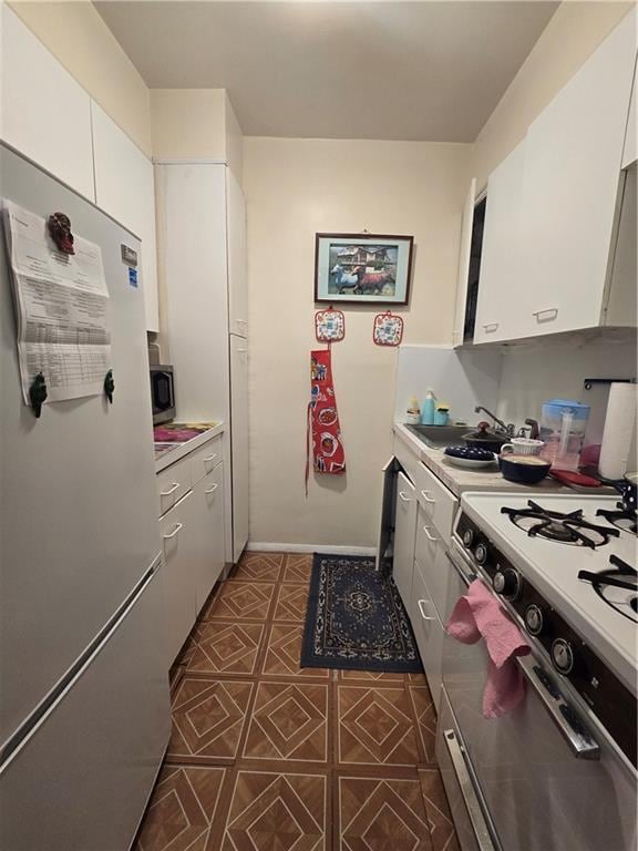 kitchen featuring range with gas cooktop, light countertops, stainless steel microwave, freestanding refrigerator, and white cabinetry