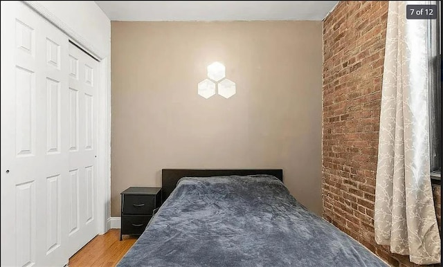 bedroom featuring a closet, hardwood / wood-style floors, and brick wall