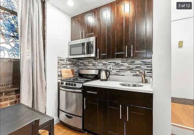 kitchen with light wood-type flooring, stainless steel appliances, dark brown cabinetry, decorative backsplash, and sink