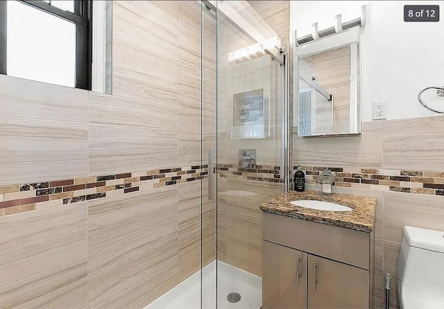 bathroom with tile walls, vanity, toilet, and a shower with shower door