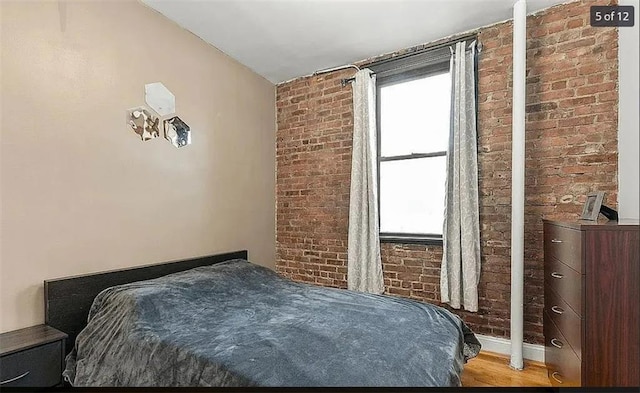 bedroom with light wood-type flooring and brick wall