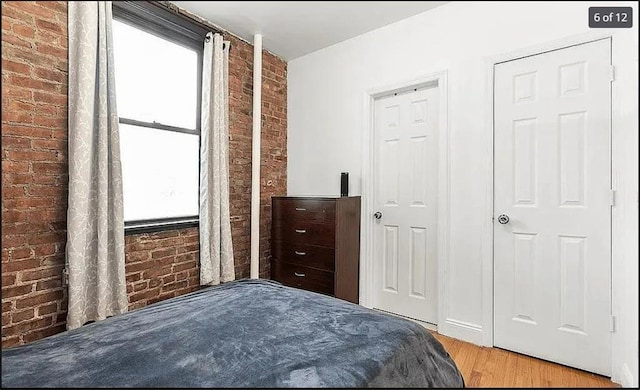 bedroom featuring light hardwood / wood-style flooring and brick wall