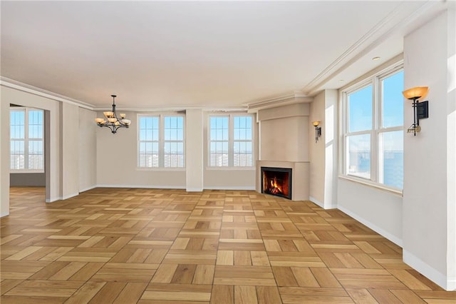 unfurnished living room with a healthy amount of sunlight, baseboards, ornamental molding, a lit fireplace, and a chandelier