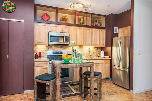 kitchen with stainless steel appliances, light countertops, backsplash, light brown cabinetry, and baseboards