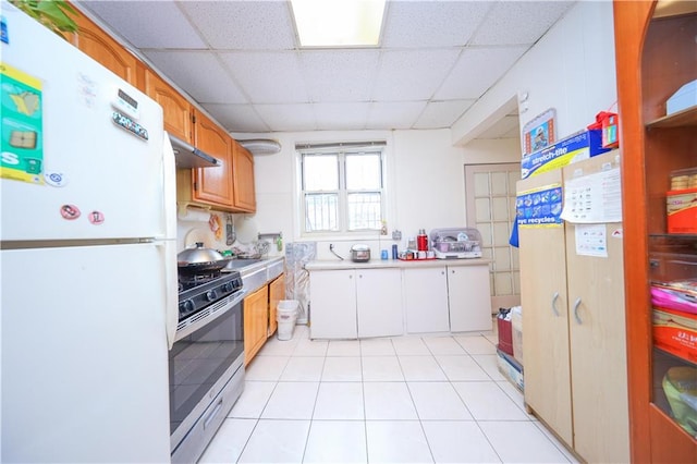 kitchen with stainless steel gas range oven, under cabinet range hood, a drop ceiling, light countertops, and freestanding refrigerator