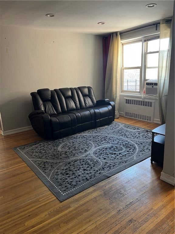 living area with wood finished floors, baseboards, cooling unit, and radiator
