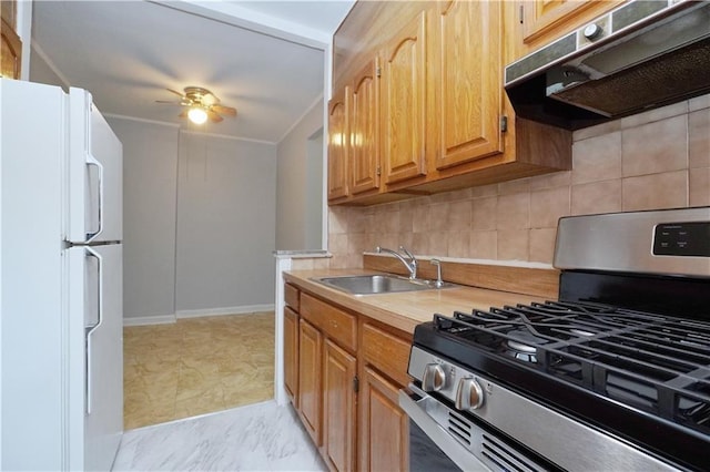 kitchen with a sink, freestanding refrigerator, gas range, under cabinet range hood, and backsplash