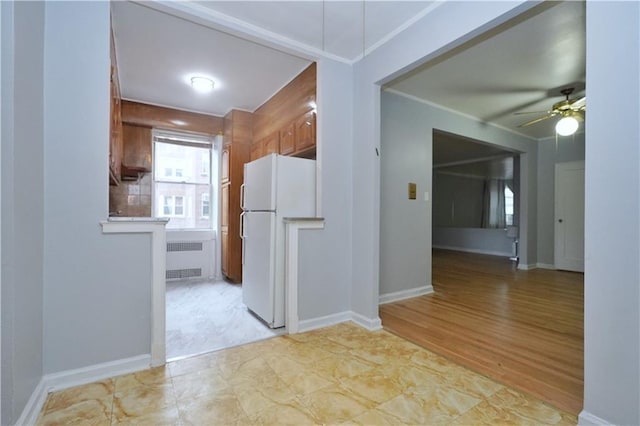 interior space featuring brown cabinets, a ceiling fan, radiator heating unit, ornamental molding, and freestanding refrigerator