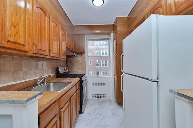 kitchen featuring radiator heating unit, freestanding refrigerator, stainless steel gas range, light countertops, and a sink