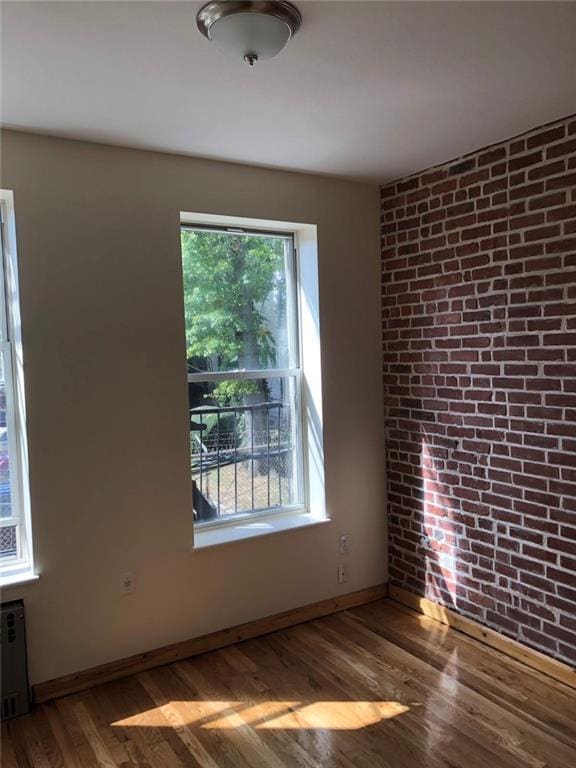 empty room with radiator, hardwood / wood-style flooring, and brick wall