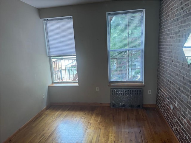 empty room with brick wall, dark wood-type flooring, and radiator heating unit