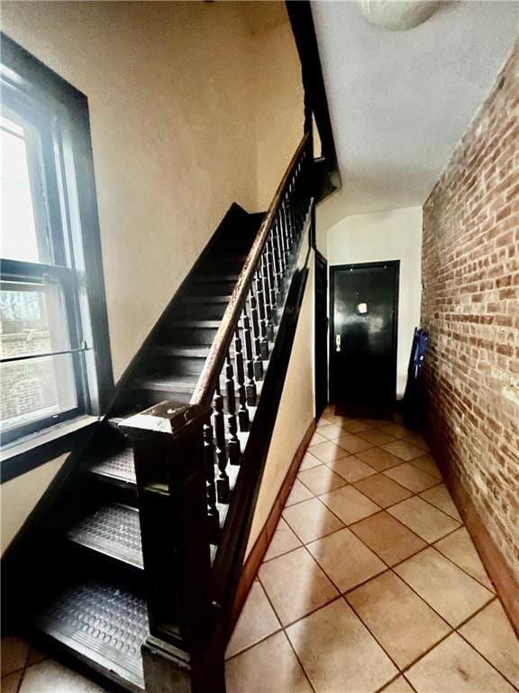 stairs with tile patterned floors and brick wall